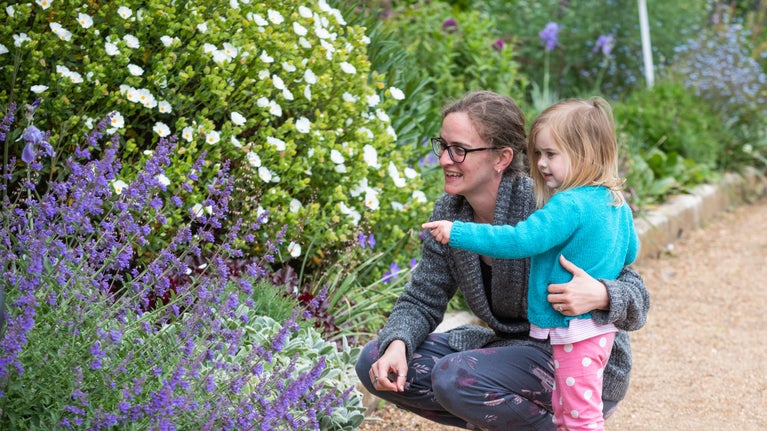 A close up of a woman and child looking at plants in a flower border